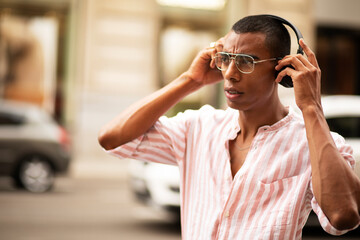 Cheerful guy with the headphones. Young african man listening the music outdoors..