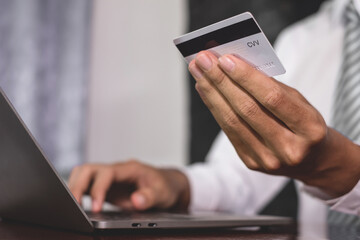 The businessman's hand is holding a credit card and using a laptop for online shopping and internet payment