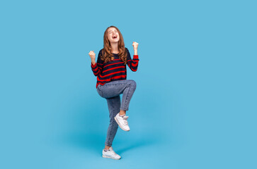 Full length positive satisfied woman wearing striped casual style sweater and jeans, raised...
