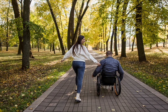 Playful girlfriend running with boyfriend sitting in wheelchair at park
