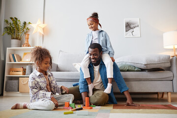 Full length portrait of two little African-American girls playing with father on floor in cozy home interior, copy space