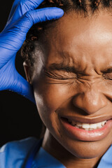 Black young doctor with headache grimacing and holding her head