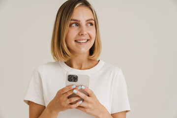 Young blonde woman smiling while using mobile phone