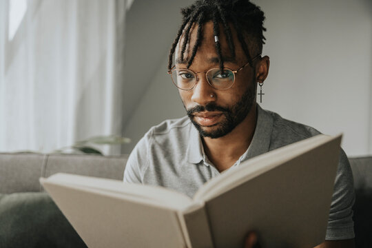 Young man wearing eyeglasses holding book at home
