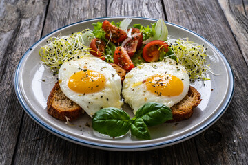 Sunny side up eggs on toasted bread, parmesan and fresh vegetables on wooden table
