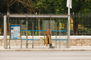 Woman in trench coat waiting at bus stop