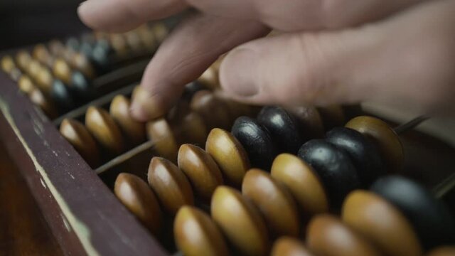 Mature man calculating with finger on wooden vintage abacus close view. Financial and cost accounting concept.