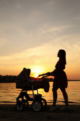 Happy mother with baby in stroller walking near river at sunset
