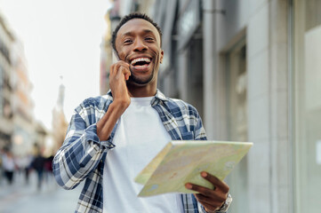 Cheerful man holding map and talking on mobile phone in city