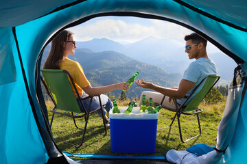 Couple and cool box with bottles of beer in mountains, view from tent