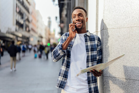 Smiling tourist with map talking on smart phone at city street
