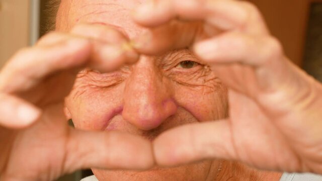 Porter of active cheerful Caucasian male over 70 showing heart shaped gesture with hands. Real people. Pensioner cheerful home leisure. Hands in the shape of a heart grandfather shows .selective focus