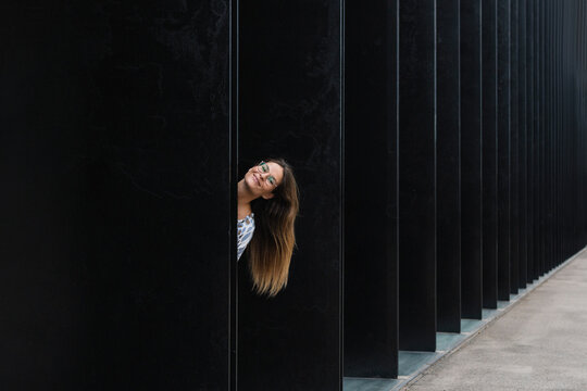Smiling businesswoman with long hair peeking from wall