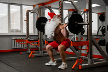 Santa claus in the gym. Muscular man with a naked torso doing exercises with dumbbells.