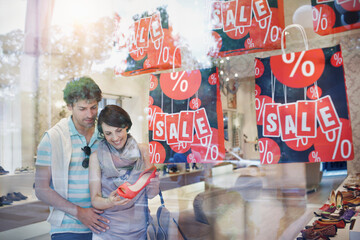 Smiling woman holding sandal while shopping with boyfriend in shoe store