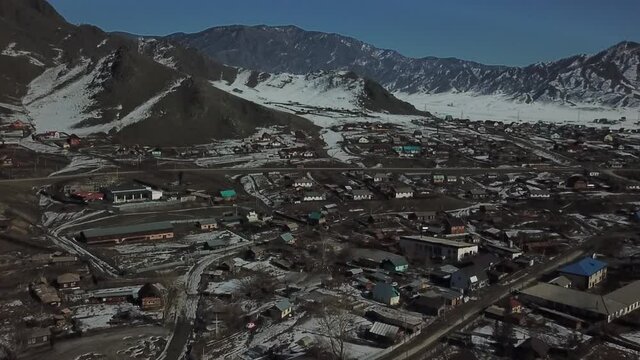 Aerial shot in forward camera movement of spring mountains. Village with melted snow and riding cars in front of mountains