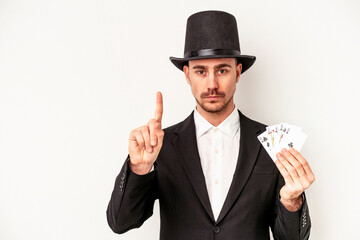 Young caucasian wizard man holding a magic cards isolated on white background showing number one with finger.