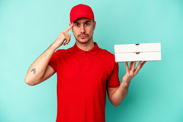 Young delivery man taking pizzas isolated on blue bakcground showing a disappointment gesture with forefinger.