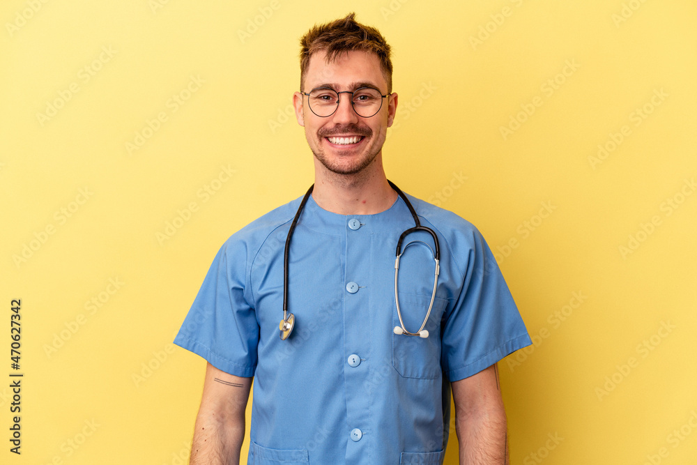 Wall mural Young nurse caucasian man isolated on yellow background happy, smiling and cheerful.