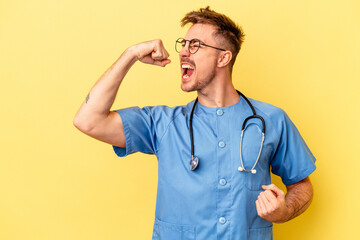 Young nurse caucasian man isolated on yellow background raising fist after a victory, winner concept. - obrazy, fototapety, plakaty