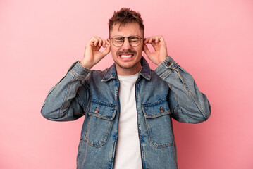 Young caucasian man isolated on pink background covering ears with hands.