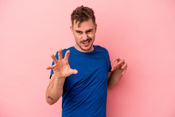 Young caucasian man isolated on pink background showing claws imitating a cat, aggressive gesture.