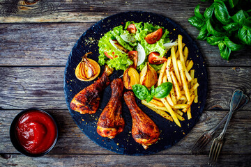 Barbecue chicken drumsticks with chips and greens  on wooden table
