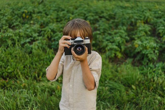 Boy photographing through vintage camera on field