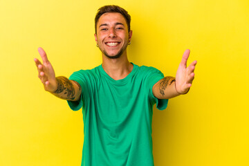 Fototapeta premium Young caucasian man with tattoos isolated on yellow background feels confident giving a hug to the camera.