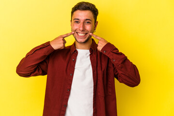 Young caucasian man with tattoos isolated on yellow background  smiles, pointing fingers at mouth.