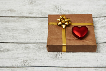 Gift box with bow ribbon and red heart on wooden background