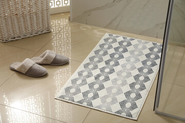Soft bath mat and slippers on floor indoors