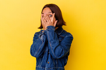 Young mixed race woman isolated on yellow background blink through fingers frightened and nervous.