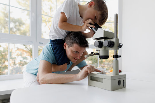 Curious boy using microscope while sitting on father's shoulders at home