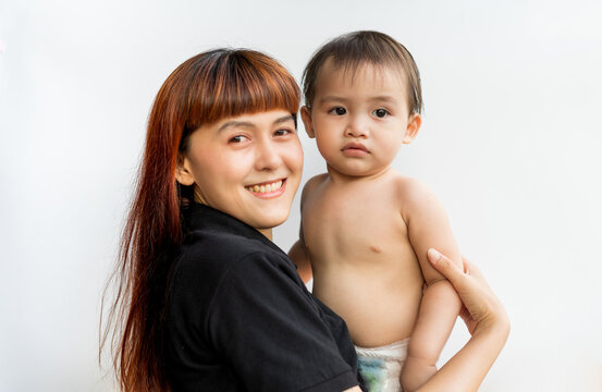 Happy mother with her baby on isolated white background. Mom wearing black shirt holding her son and smiling merrily. Young attractive happy mother smiling hugging looking at her littel baby.