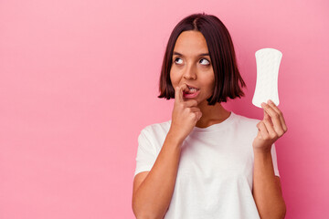 Young mixed race woman holding a compress isolated on pink background relaxed thinking about something looking at a copy space.