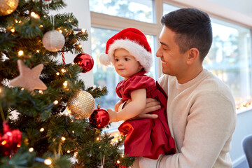 winter holidays and family concept - happy middle-aged father and baby daughter decorating christmas tree at home