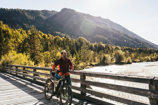 Smiling man wheeling mountain bike on bridge