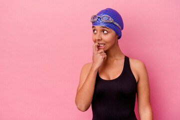 Young swimmer mixed race woman isolated on pink background relaxed thinking about something looking at a copy space.