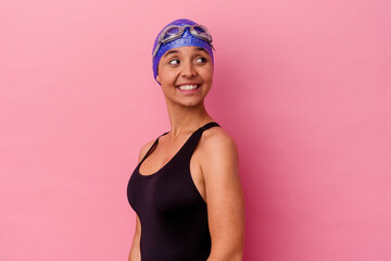 Obraz na płótnie Canvas Young swimmer mixed race woman isolated on pink background looks aside smiling, cheerful and pleasant.