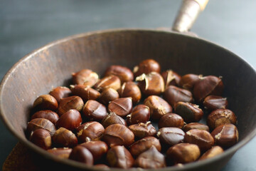 Pan filled with chestnuts on dark background. Selective focus.