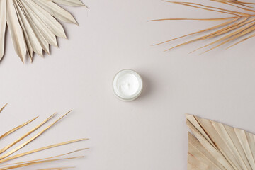 Jar of cosmetic cream with palm leaf on grey background. Flat lay