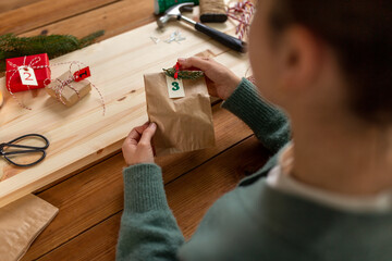 winter holidays and hobby concept - hands with clothespin, craft paper bag and tag making advent...