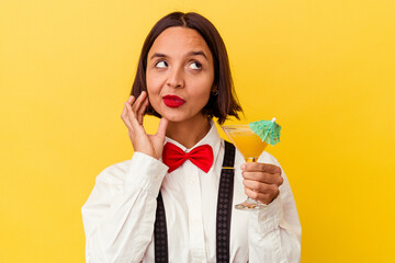 Young pretty bartender woman holding a cocktail on a yellow background