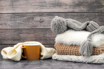 Beige mug wrapped in a white scarf and winter clothes on the table