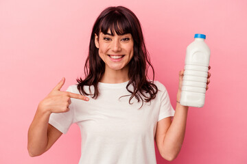Young caucasian woman holding a bottle of milk isolated on pink background person pointing by hand to a shirt copy space, proud and confident