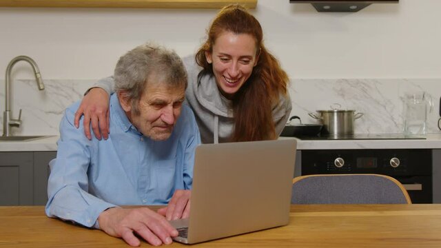 Happy grandfather and daughter hugging looking at something on a laptop at home. Smiling two generations family members or relatives having positive emotion