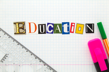 Education - word from cutting magazine clippings on white checkered notebook sheet of paper background with ruler, highlighter and markers pen. Education title concept.