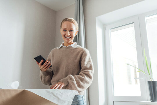 Happy woman with mobile phone and plan in new apartment