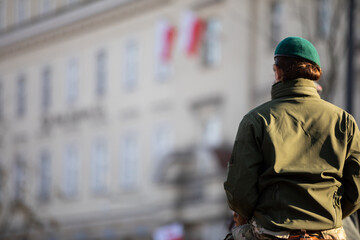 An army woman in uniform and green beret in the background of a building.